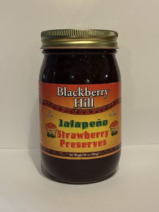 Close-up of a dark glass jar with a gold screw-top lid; label reads 'Blackberry Hill Jalapeño Strawberry Preserves.'